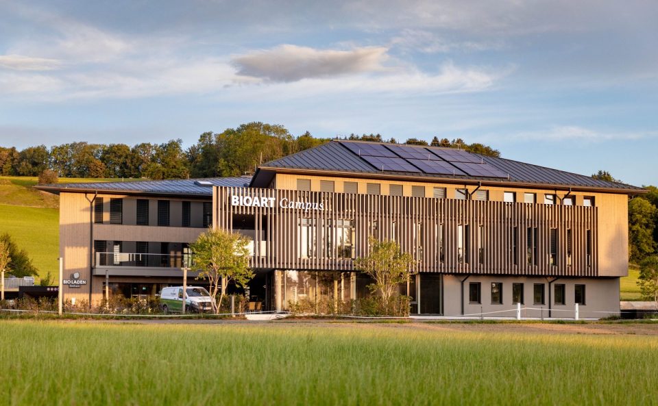 Holzfassade des BioArt Campus in Seeham im Abendlicht, davor eine Wiese