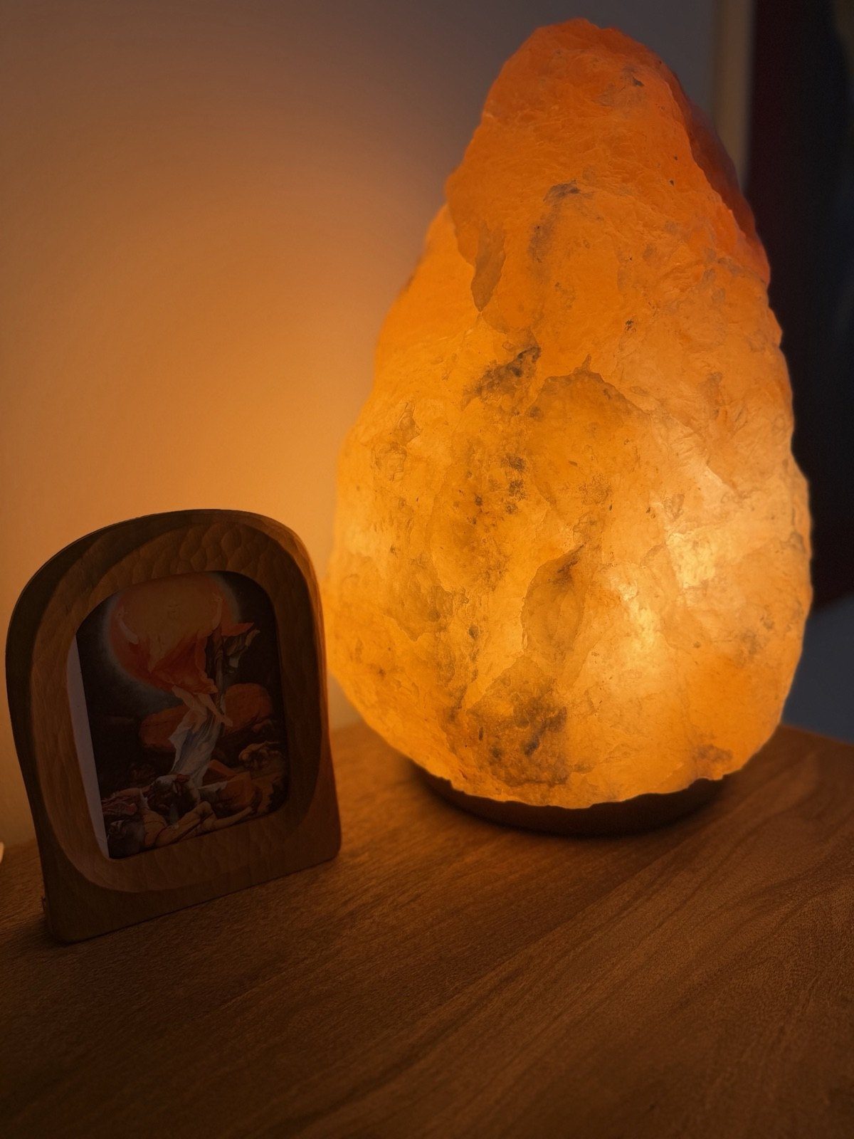 Leuchtende Salzkristall-Lampe auf einer Holzkommode neben einem kleinen Bild im Holzrahmen