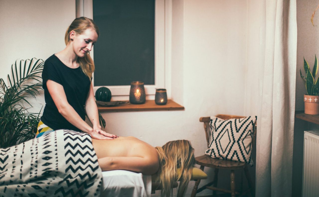 Massage bei Körperwerk: Eine Therapeutin massiert den Rücken einer liegenden Person in einem warm beleuchteten Raum