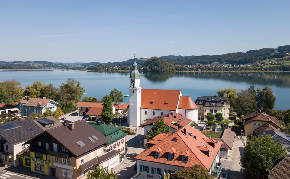 Seeham von oben: Ortskern mit der Pfarrkirche, dahinter der Obertrumer See und bewaldete Hügel